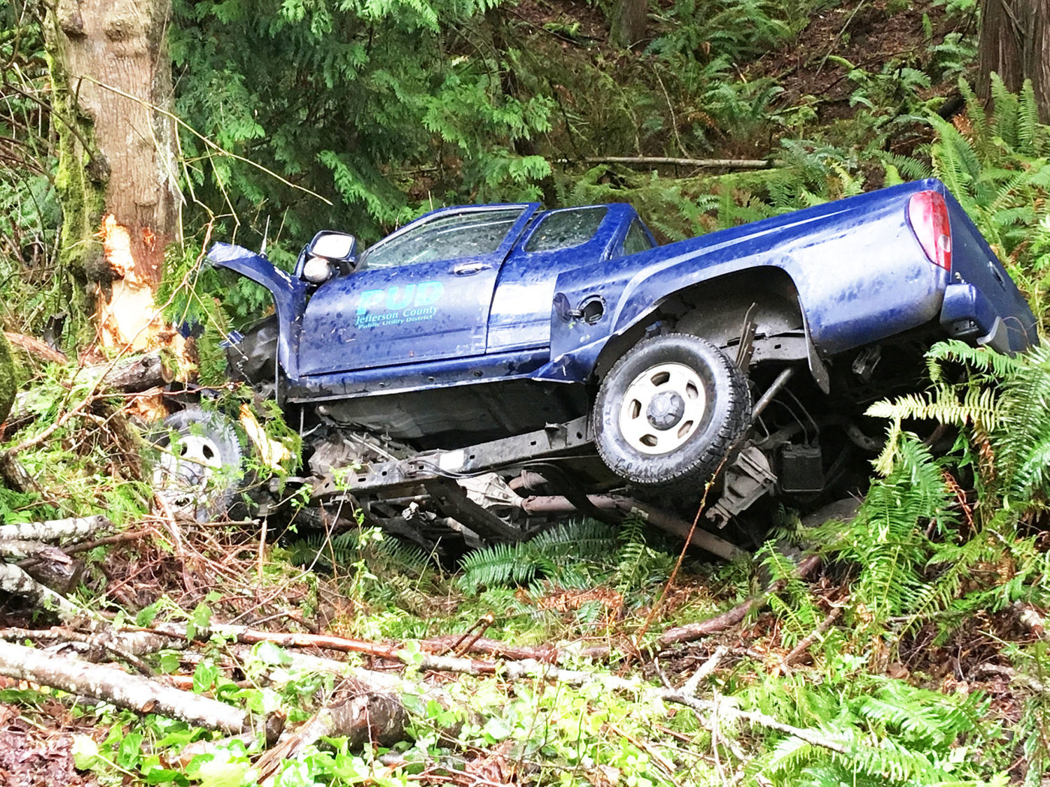 RIGHT: A truck driven by a 72-year-old Jefferson County Public Utility District employee is seen to the left in a ravine off State Route 20. The man died April 16 when the vehicle he was driving drifted off the highway and struck a guardrail, then traveled down an embankment.