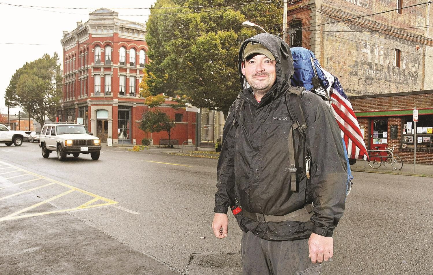 Eli Smith, who is hiking to all four corners of the U.S., stands in downtown Port Townsend with his 60-pound backpack and U.S. flag Oct. 18.