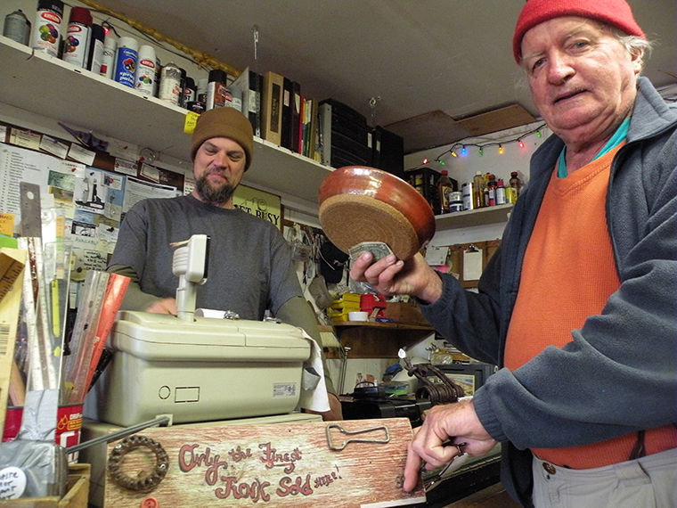 Caleb Needham, shopkeeper at Waste Not, Want Not in Port Townsend, smiles when frequent shopper Francis Brophy points to a sign below the cash register that reads “Only the Finest Junk Sold Here!” Brophy picked up two bowls last Thursday. Photo by Allison Arthur