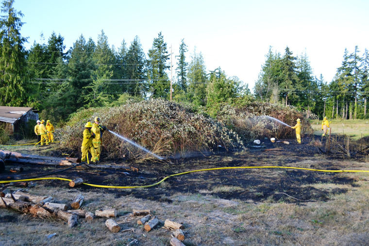 Firefighters from East Jefferson Fire Rescue and Naval Magazine Indian Island hose grass and brush in an area where a fire broke out Sunday evening after a man chopping wood on Four Corners Road tried to burn out termites in an infested log. The fire burned about one-tenth of an acre. Photo by Bill Beezley, EJFR
