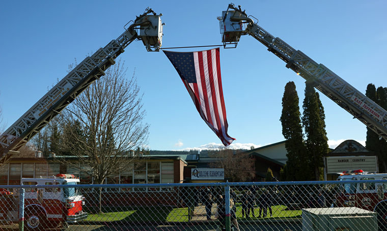An American flag hangs from two ladder trucks, one from Clallam County Fire District 3 (left) and the other from East Jefferson Fire Rescue, outside Quilcene School for a Saturday, Feb. 21 memorial service for Quilcene Fire Rescue Deputy Chief Robert "Moe" Moser. Photo by Nicholas Johnson