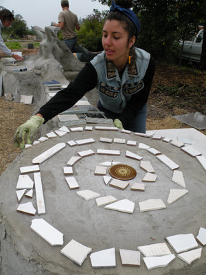 Mona May adds touches to a spiral mosaic at the end of a guitar-shaped earthbench. May didn’t know Al Nejmeh but has been traveling with Dan “Dan Dan” Schoen and others who help communities put together earthbenches. There are typically community trash pickup events with "bottle bricks" made to go into the benches.