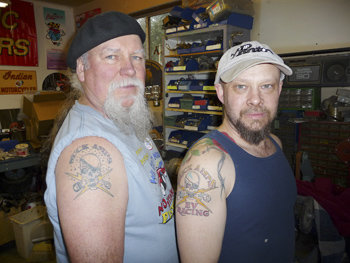 Roderick Wilde (left) and Mike Willmon, president of the National Electric Drag Racing Association, proudly display their tattoos Feb. 27 as they prepare Wilde’s 1979 Mazda RX-7 for an international drag racing competition in Croatia this June. Photo by James Robinson