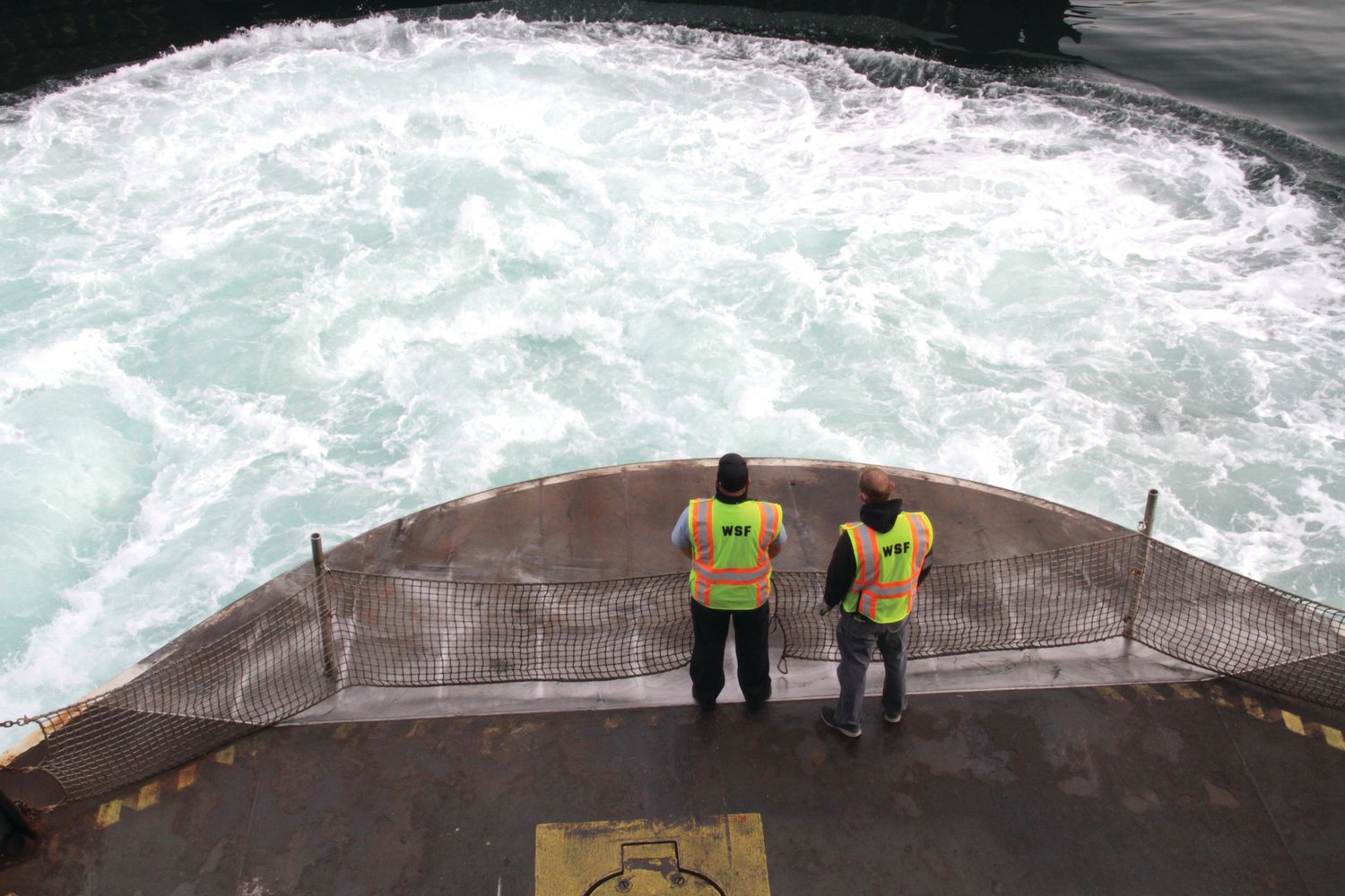 Crew members of the ferry M/V Kennewick stand at the main deck gate as the slowing vessel pushes out a white wave during its arrival Monday morning in Port Townsend.