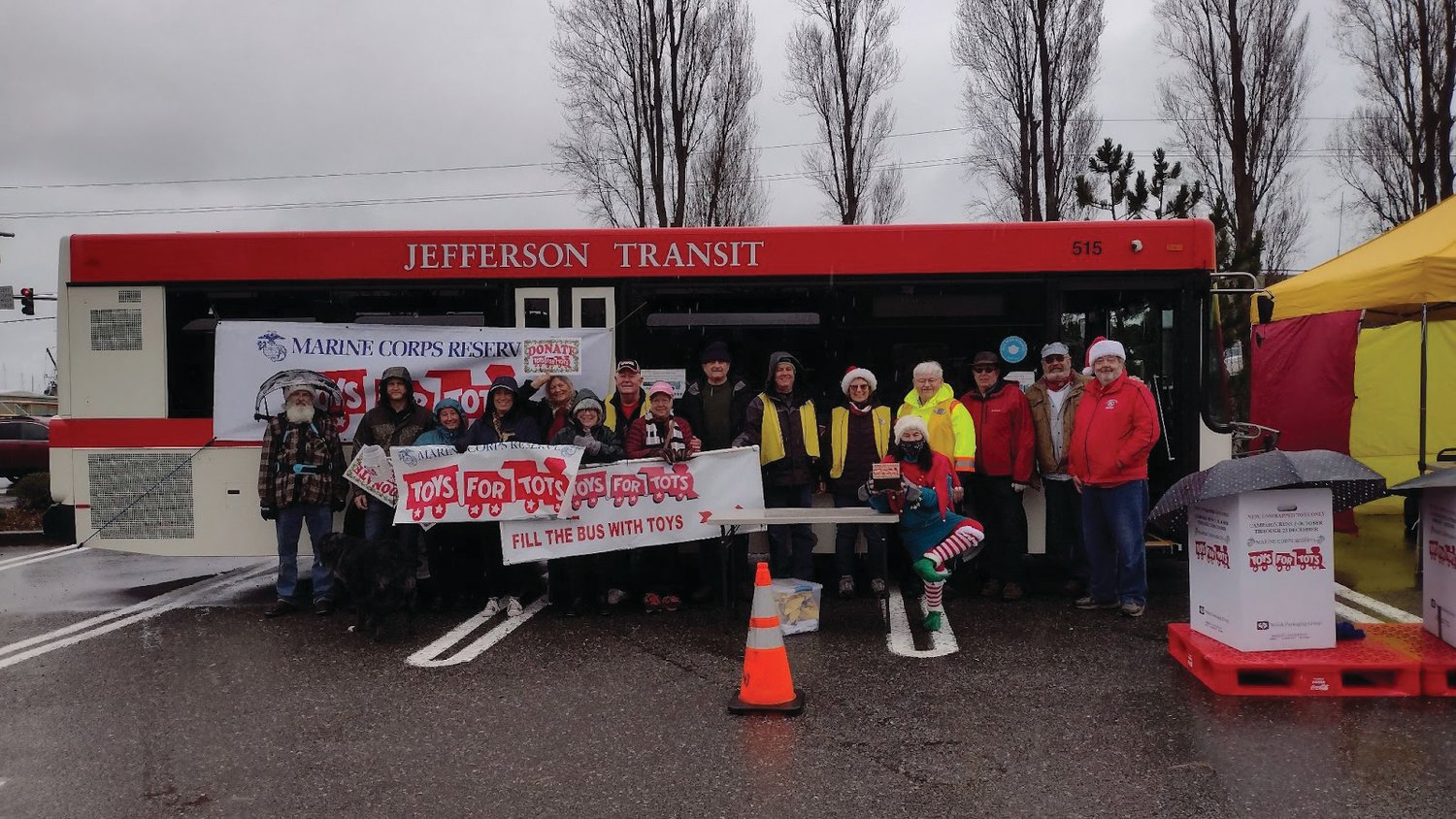 Volunteers from Toys for Tots and Jefferson County Transit stand in front of a bus ready to be stuffed with toys.