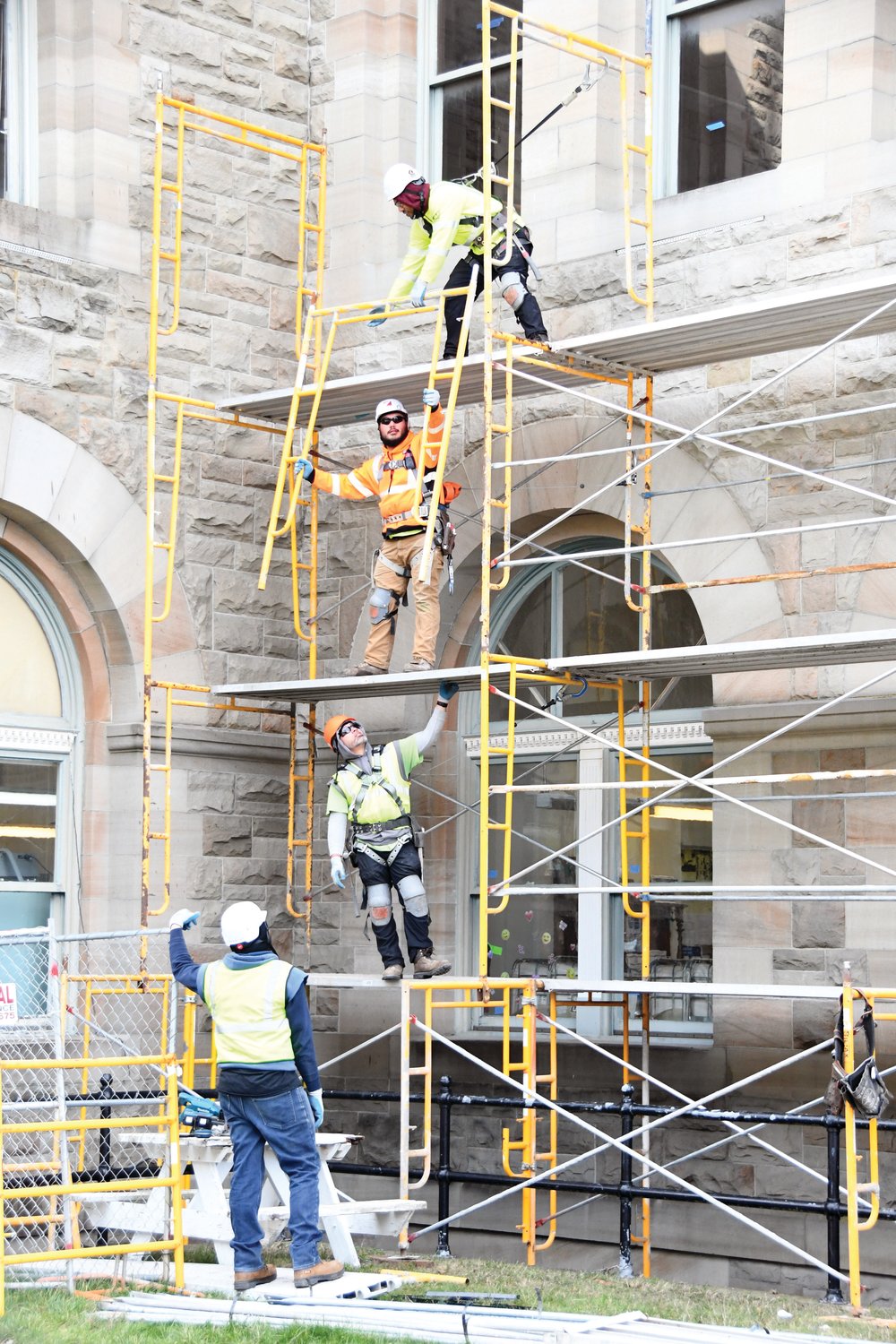Construction workers with PCI hoist scaffolding pieces on the north-facing wall of the sandstone structure in early March.